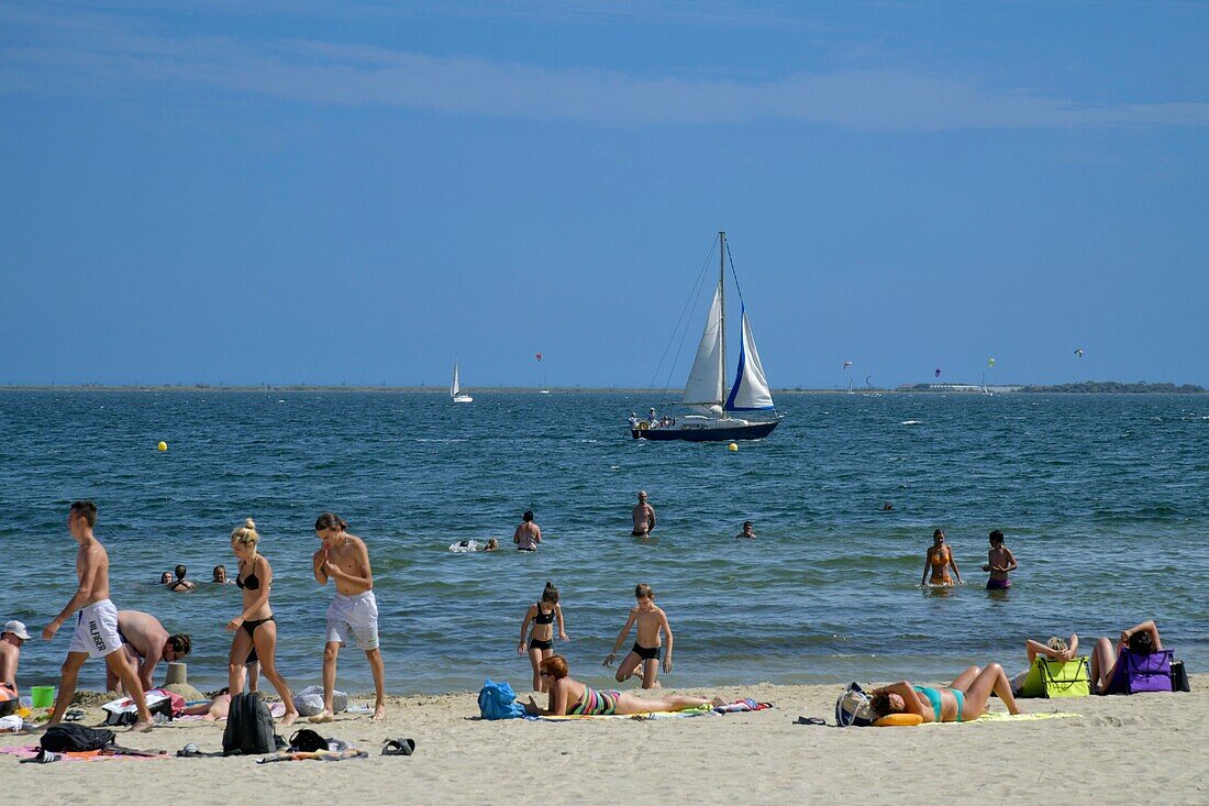 France, Herault, Meze, vacationers on a beach in the lagoon of Thau with a sailboat in the background\n