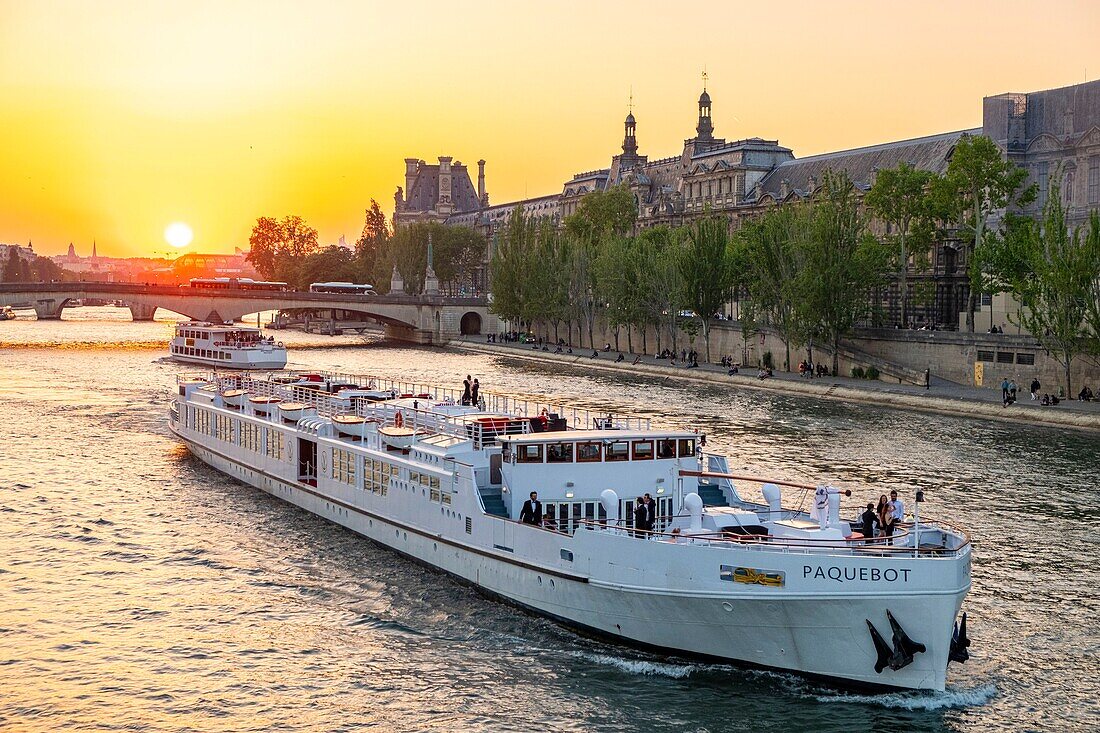 France, Paris, area listed as World Heritage by UNESCO, a festive cruise ship passes by the Louvre at sunset\n
