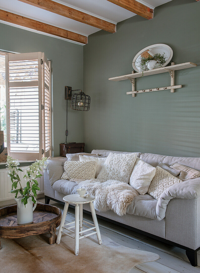 Grey sofa with cushions and fur, wall shelf and plant in country-style living room