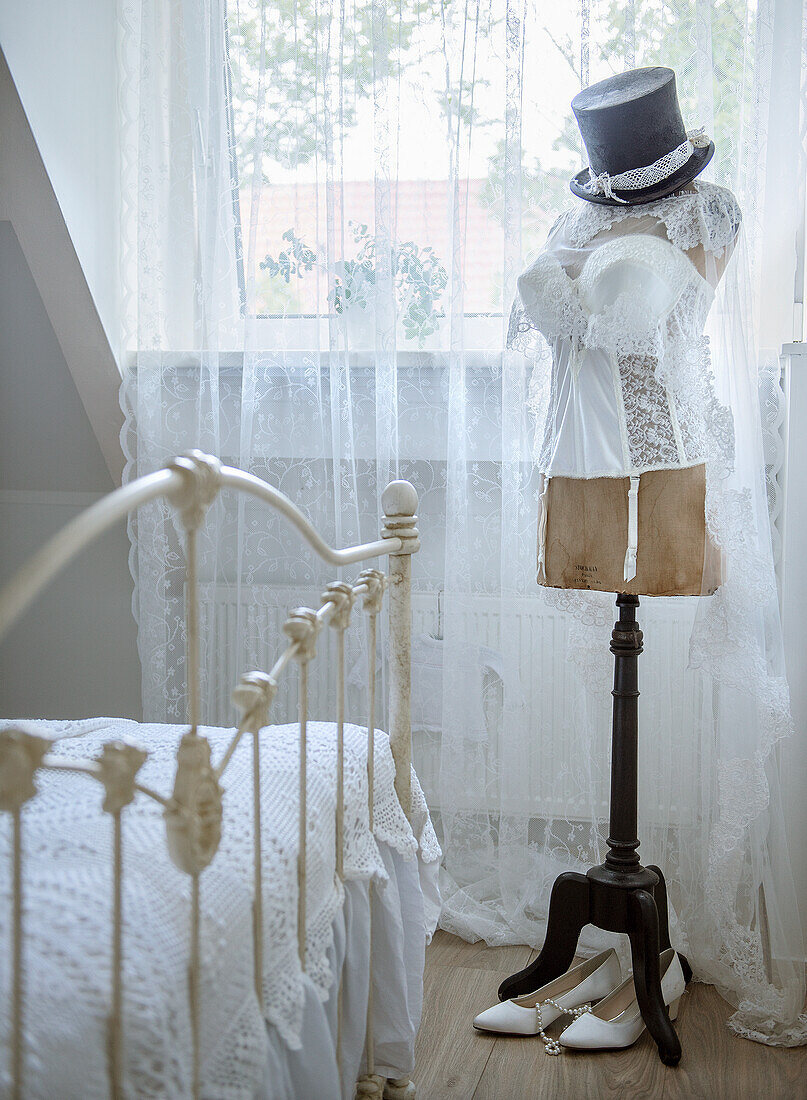 Bedroom with lace curtains, dressmaker's dummy and ornate metal bed