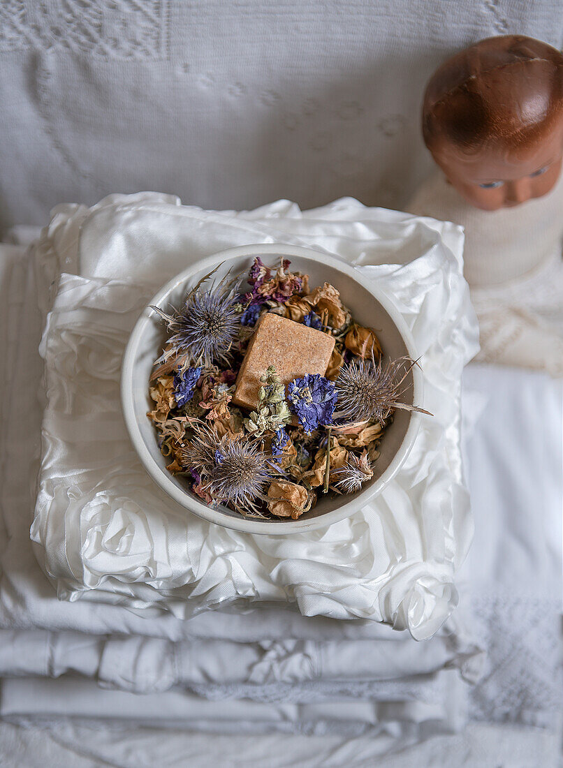 Schale mit getrockneten Blumen und Seifenstück auf gefaltetem Stoffstapel