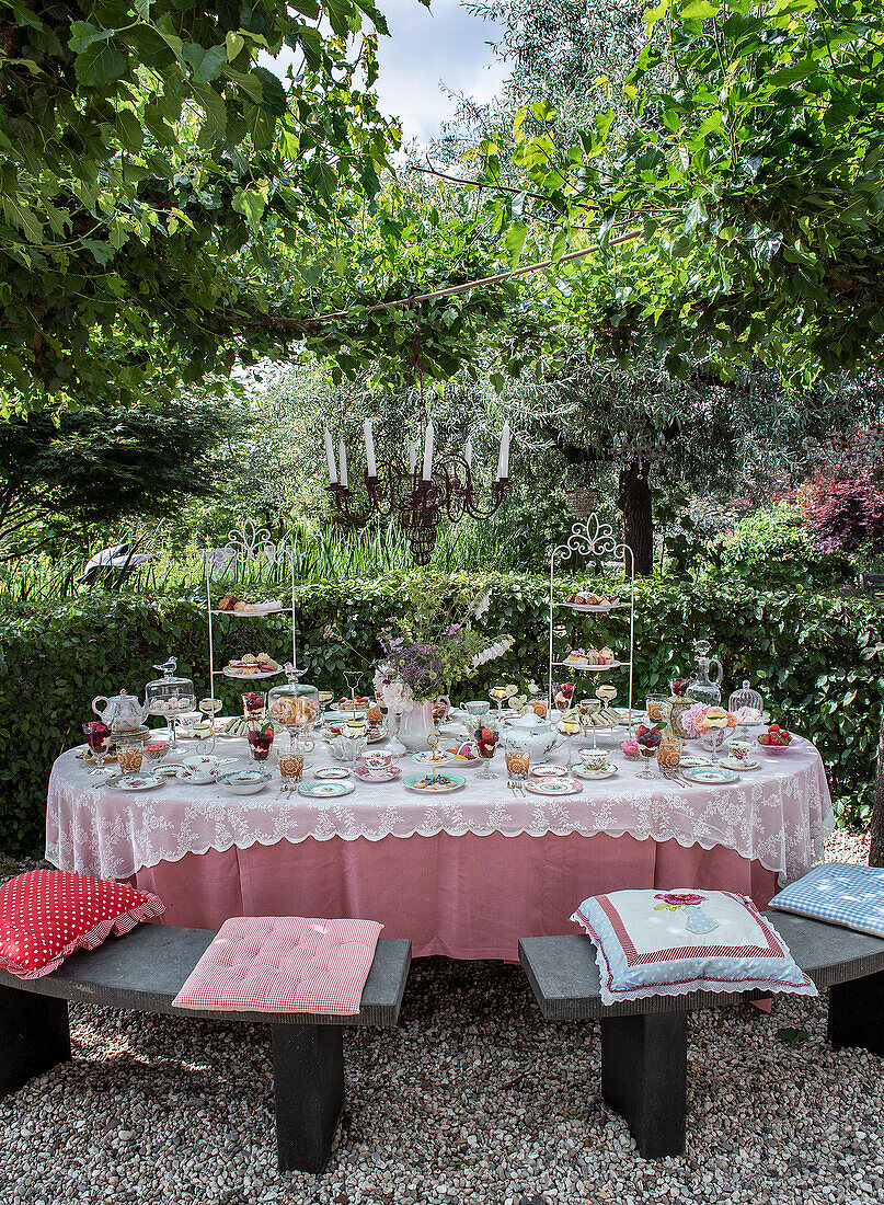 Tea table in the garden with richly laid table and chandelier