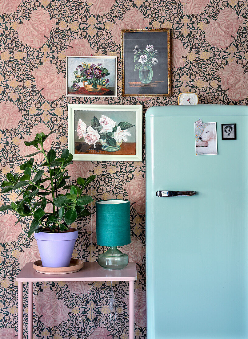 Retro-Kühlschrank und Pflanze vor floraler Tapete und Blumenbildern