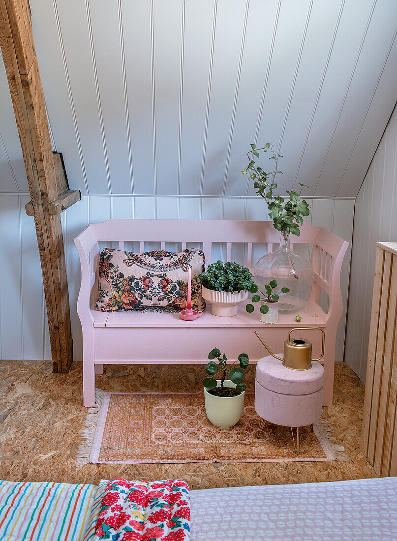 Pink bench with plants and cushions with floral pattern under sloping roof