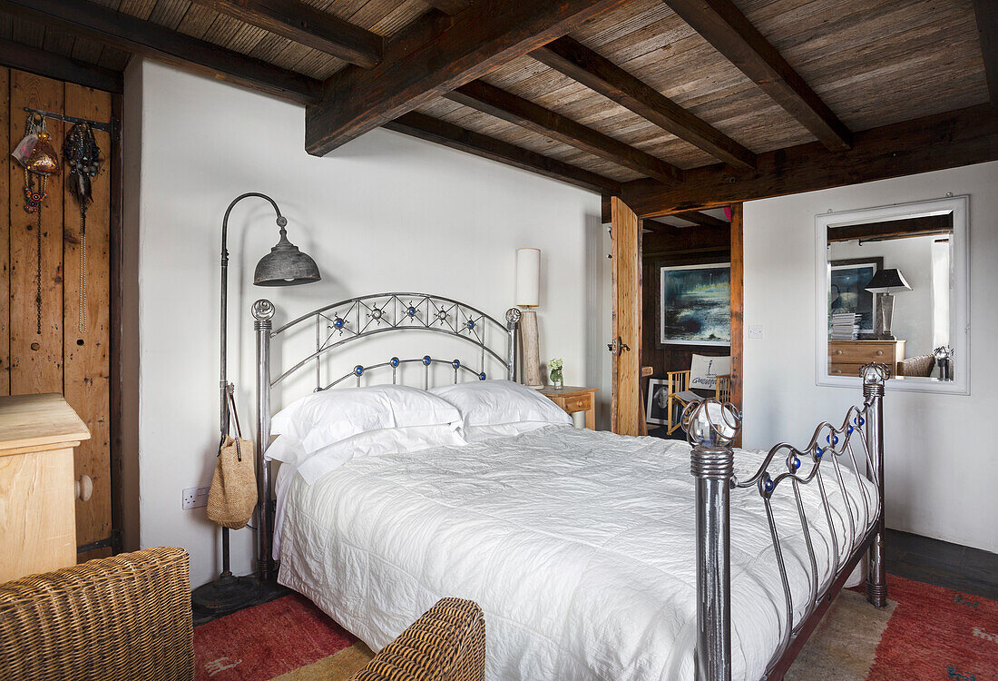 Metal bed with white bed linen in rustic bedroom with beamed ceiling