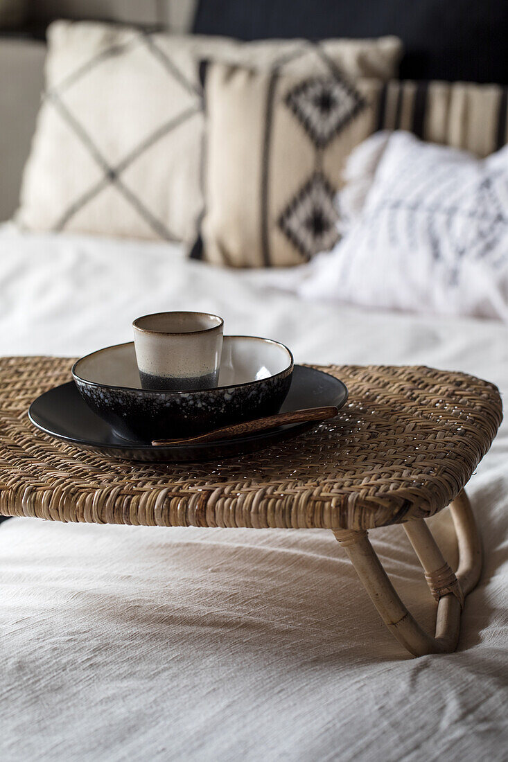 Rattan side table with ceramic crockery on white bed linen