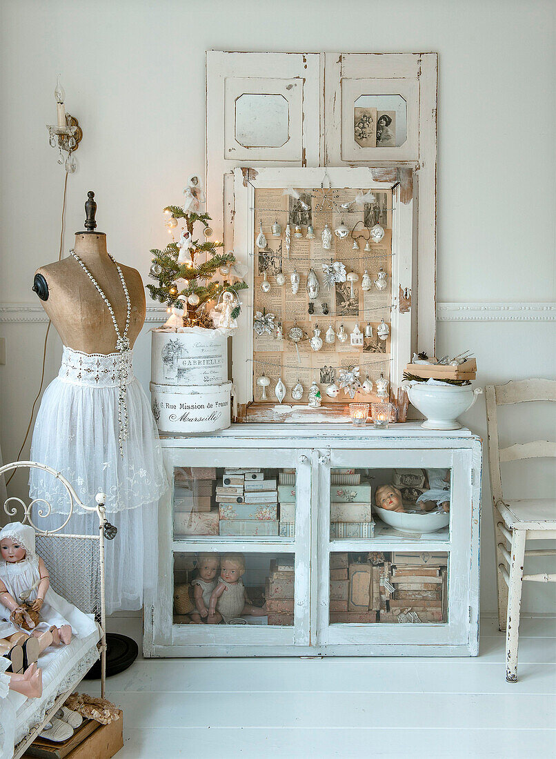 Fir tree and Christmas decorations on display cabinet and a dressmaker's dummy with lace-trimmed garment