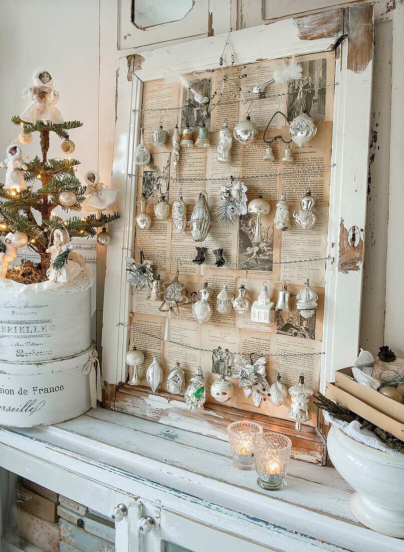 Antique Christmas tree decorations hanging in a window frame lined with old newspaper, Christmas tree in front of it