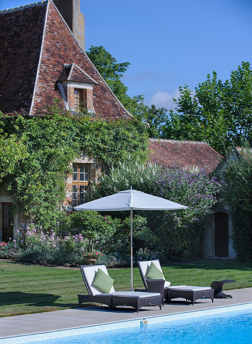 Two sun loungers with sun umbrella at the edge of the pool