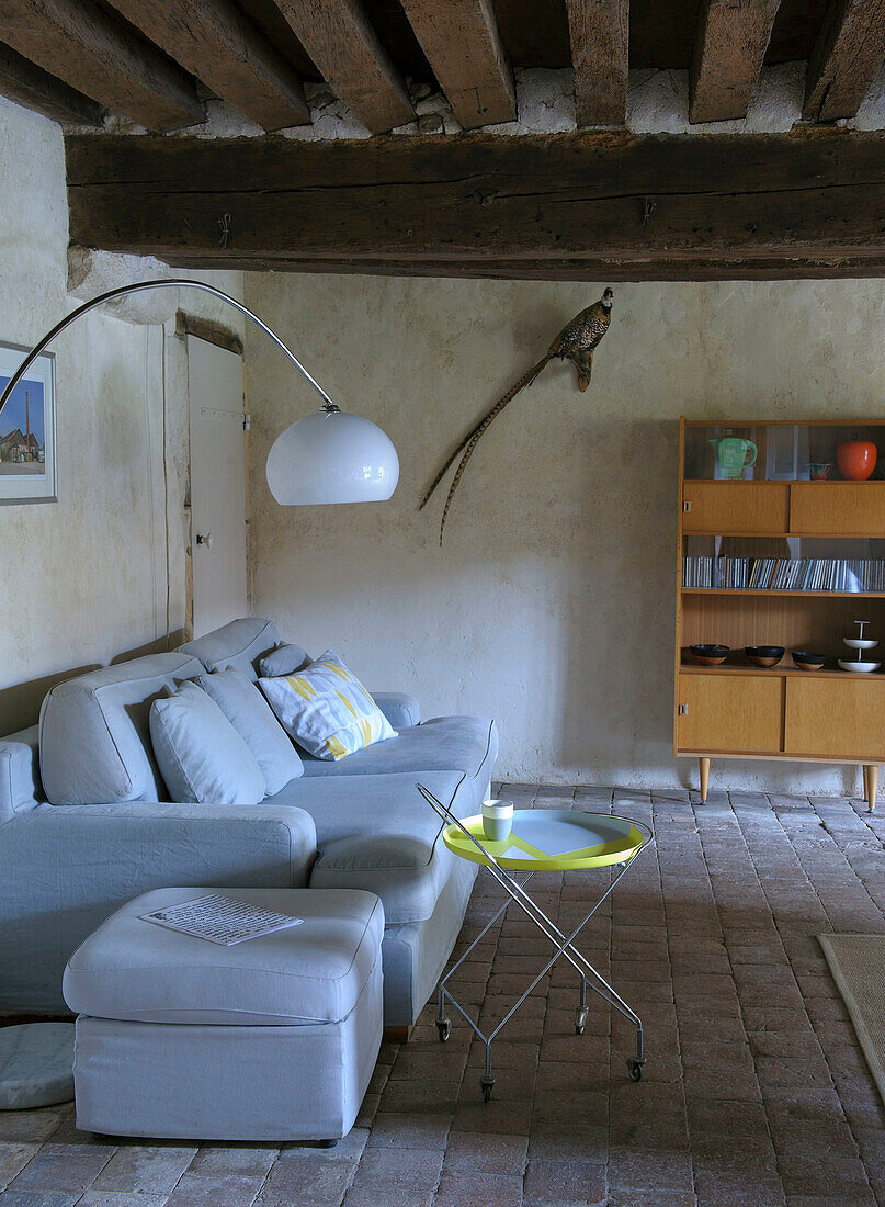 Grey upholstered sofa with ottoman and side table, mid-century bookcase in the background