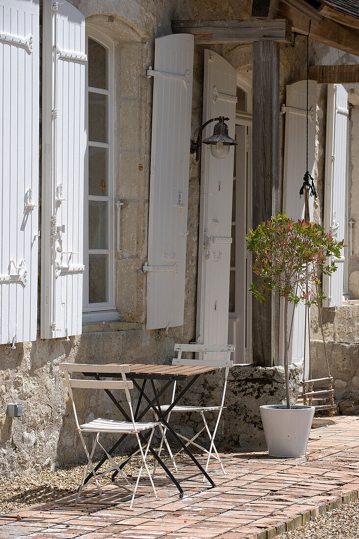 Folding table and chairs in front of traditional stone house with shutters