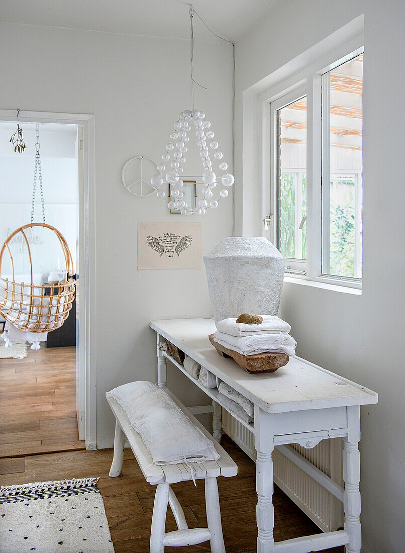 White console table with wooden bench and decoration, hanging chair in the background