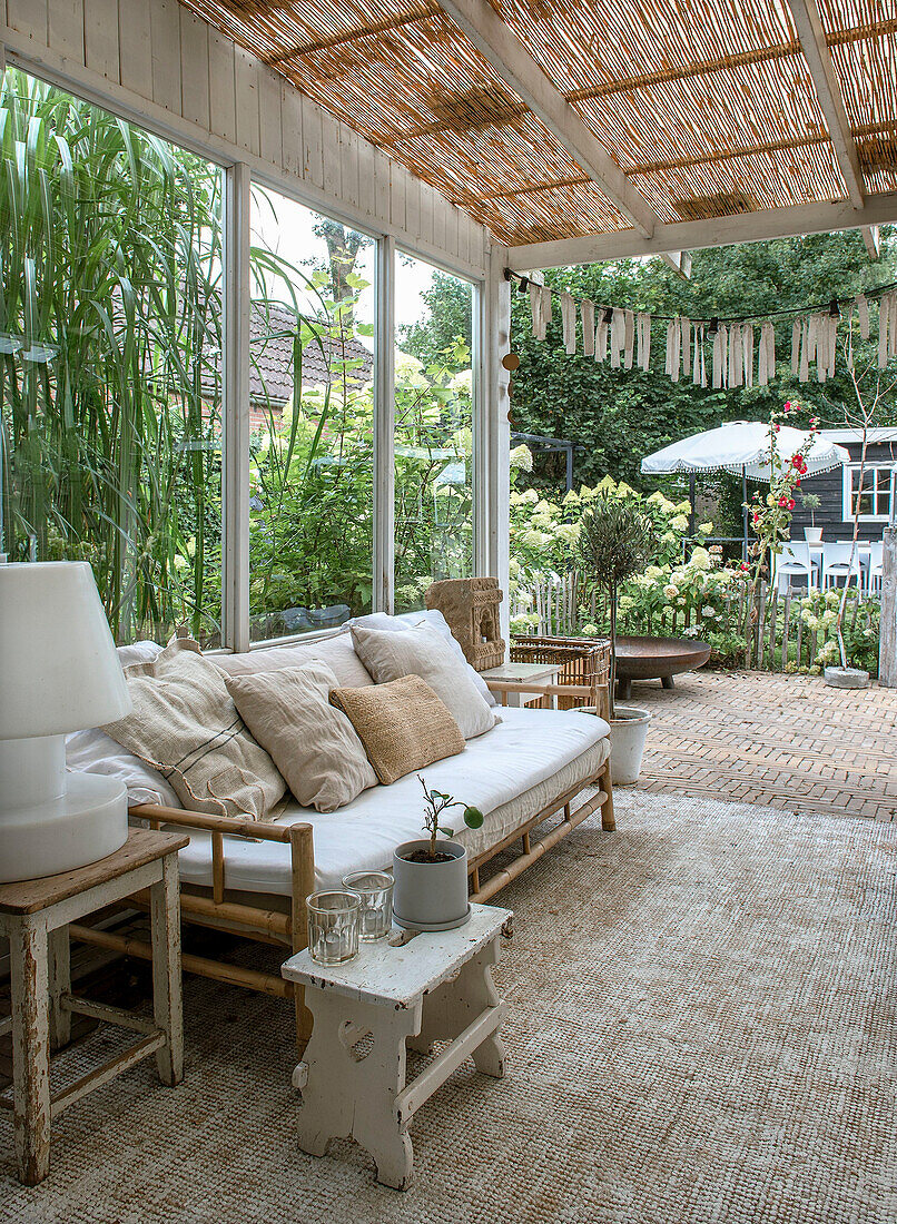 Überdachte Terrasse mit Bambus-Sofa, Kissen und Pflanzen im Hintergrund