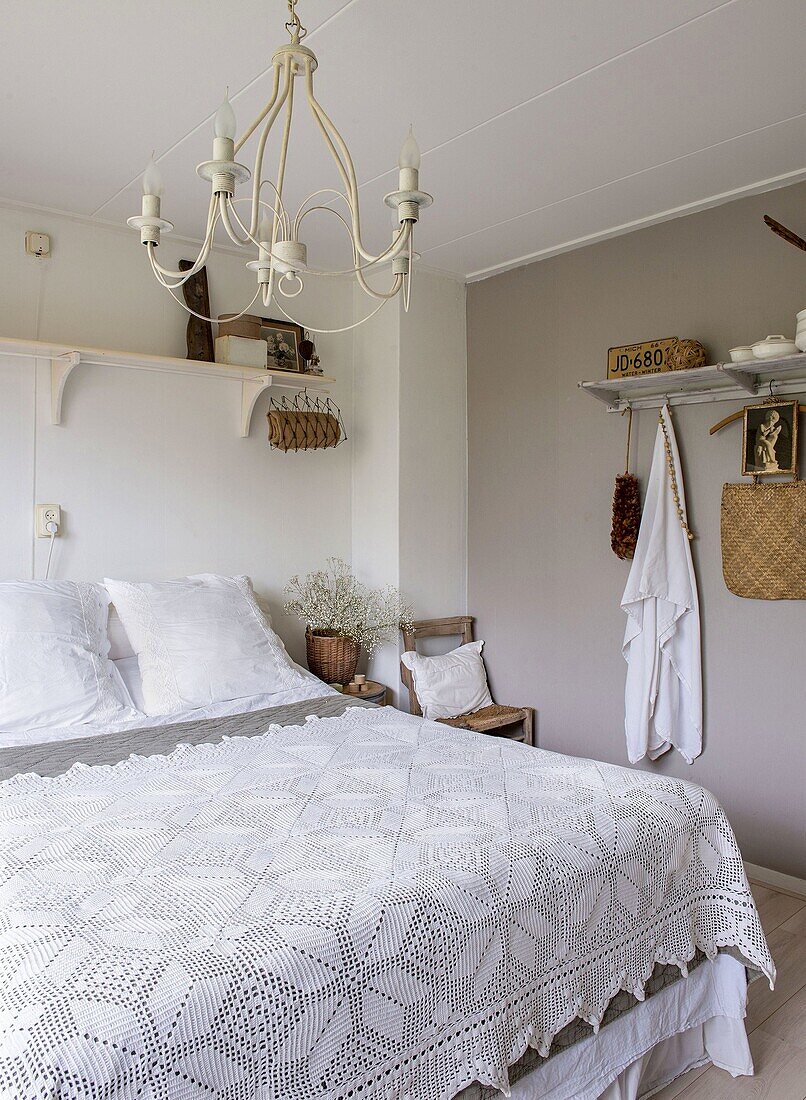 Bedroom with double bed and crocheted bedspread, white chandelier and shelves