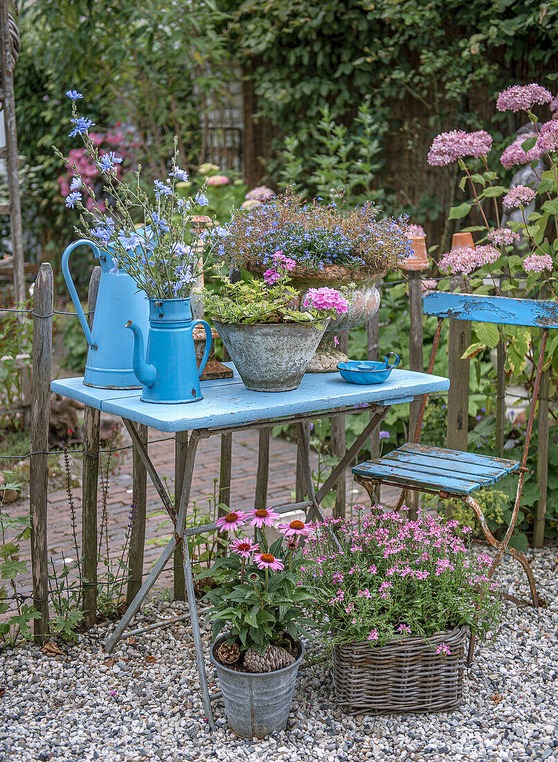 Blau gestrichener Gartentisch mit Blumenarrangement und alten Teekannen