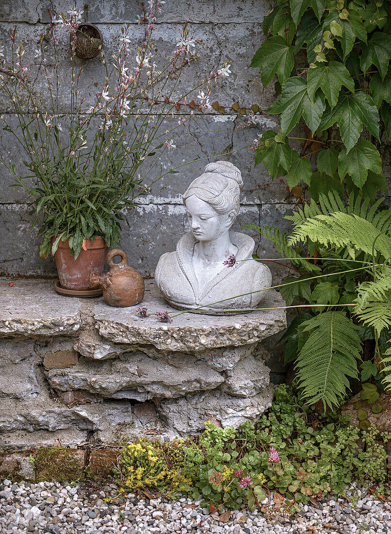 Bust on a stone pedestal, surrounded by various plants