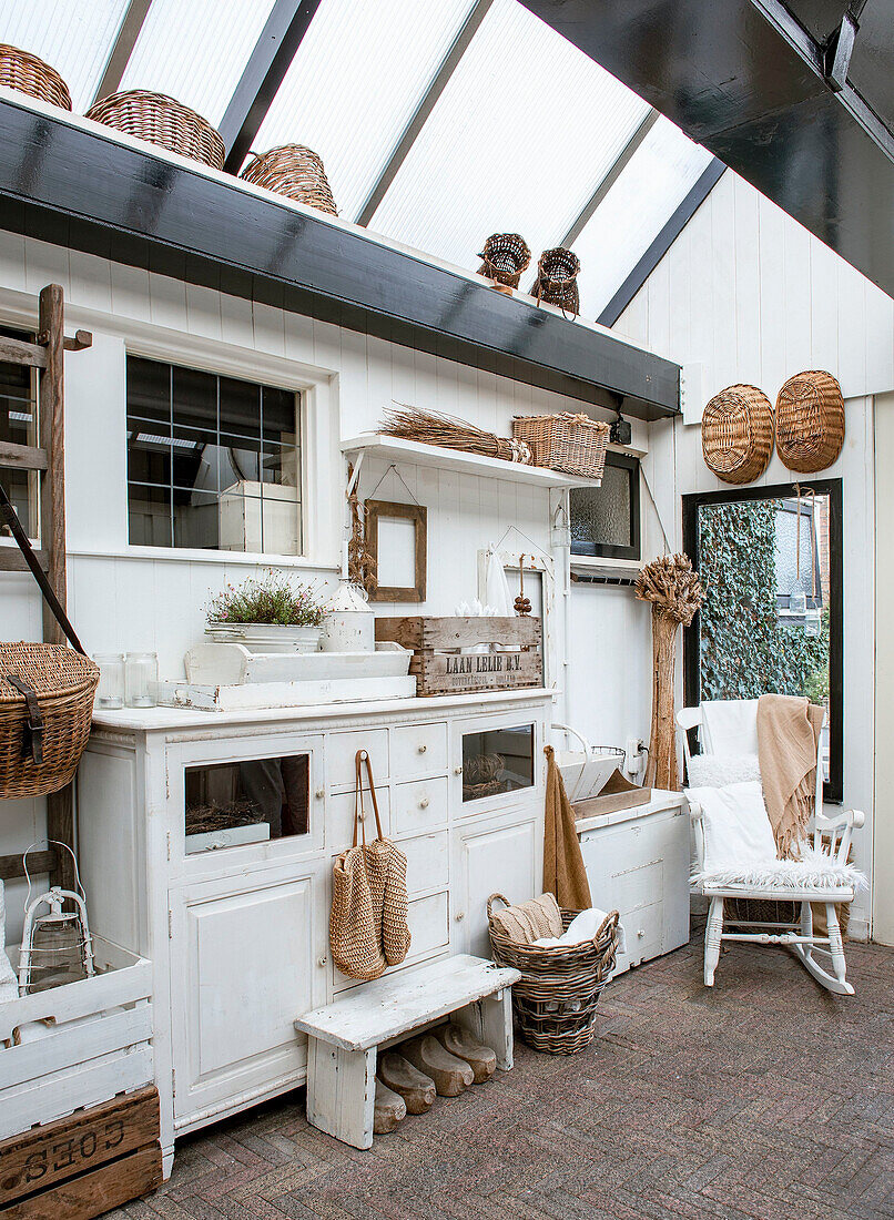 Wintergarten im Landhausstil mit weißen Möbeln, Körben und Holzdekor