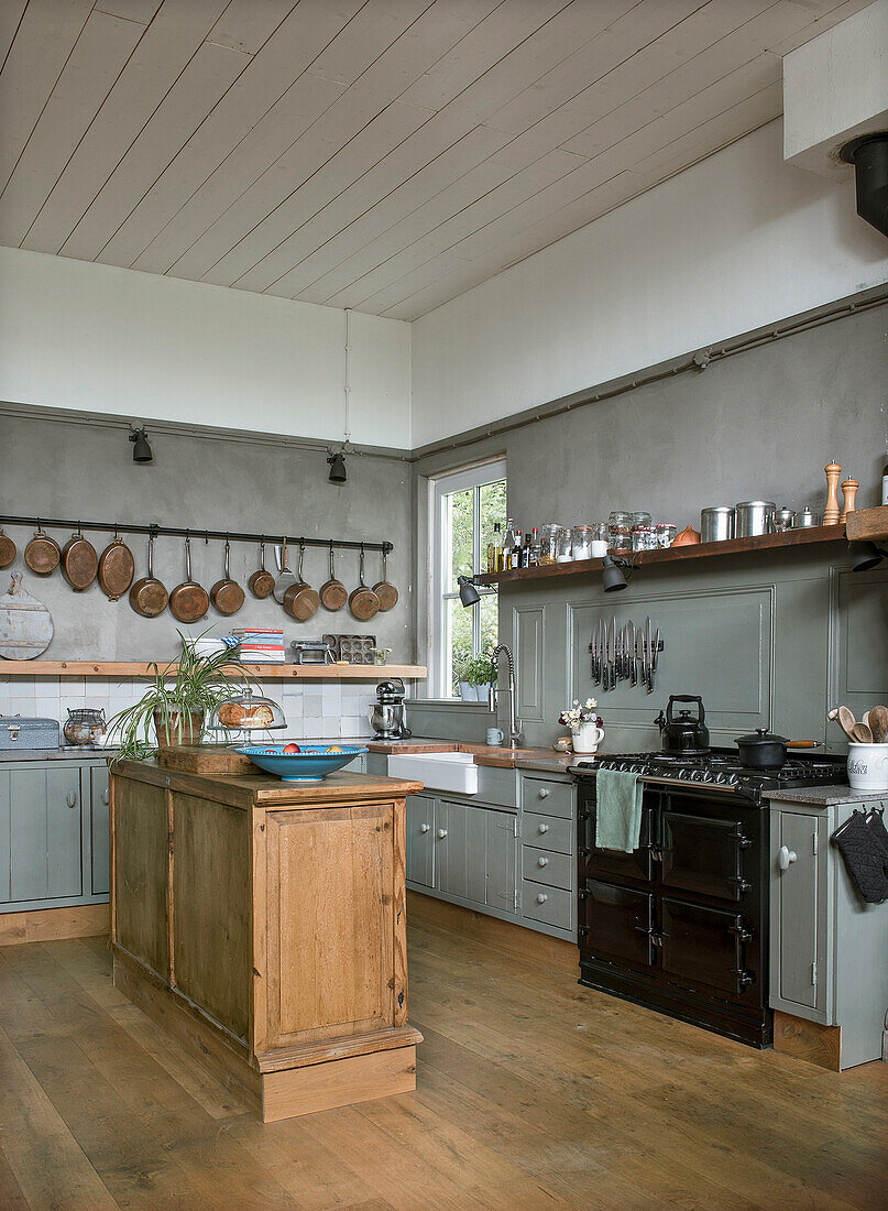 Landhausküche mit Kücheninsel aus Holz und schwarzem Herd, Kupferpfannen an der Wand