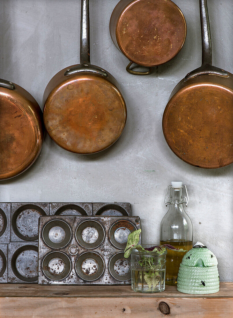 Copper pots and pans and old baking tins on grey kitchen wall