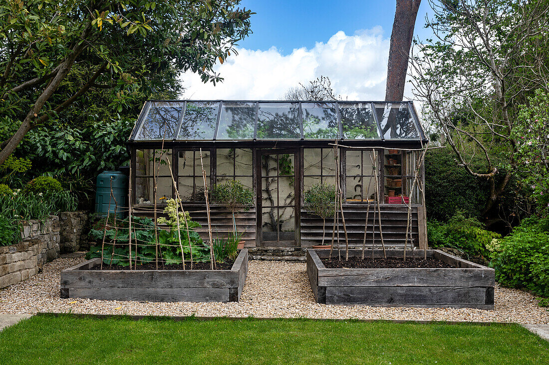 Hochbeete und Gewächshaus im Garten mit Kiesweg und Rasenfläche