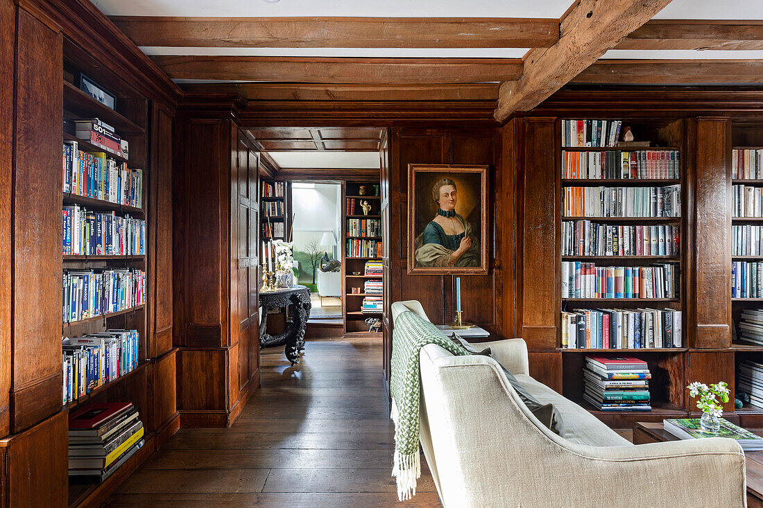 Holzbibliothek mit cremefarbenem Sofa und historischem Porträt an der Wand