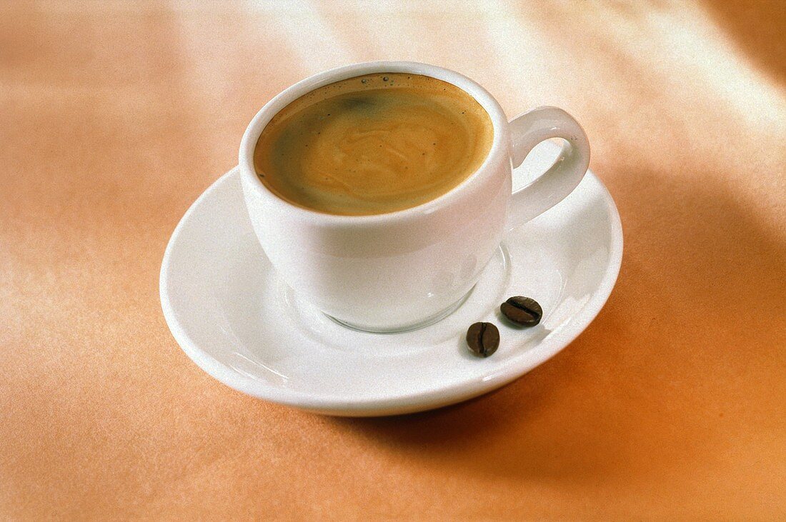 Eine Tasse Kaffee und zwei Kaffeebohnen auf dem Unterteller