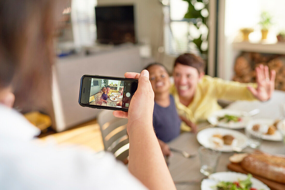 Woman photographing wife and son at dinner table