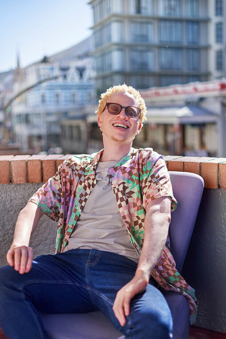 Young albino man sitting on sunny city rooftop
