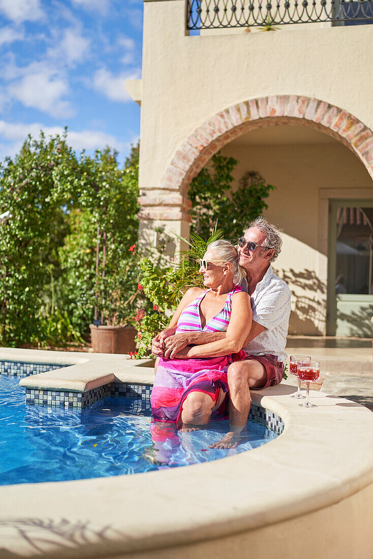Senior couple relaxing by swimming pool on villa patio