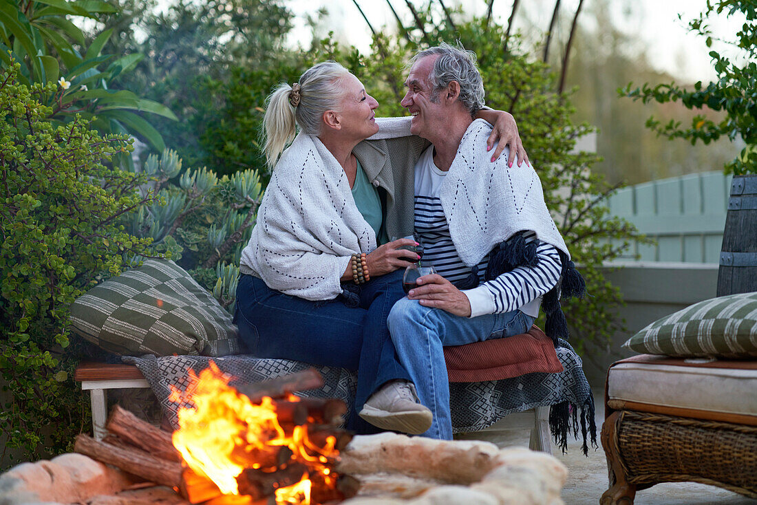 Senior couple drinking wine and hugging by fire pit