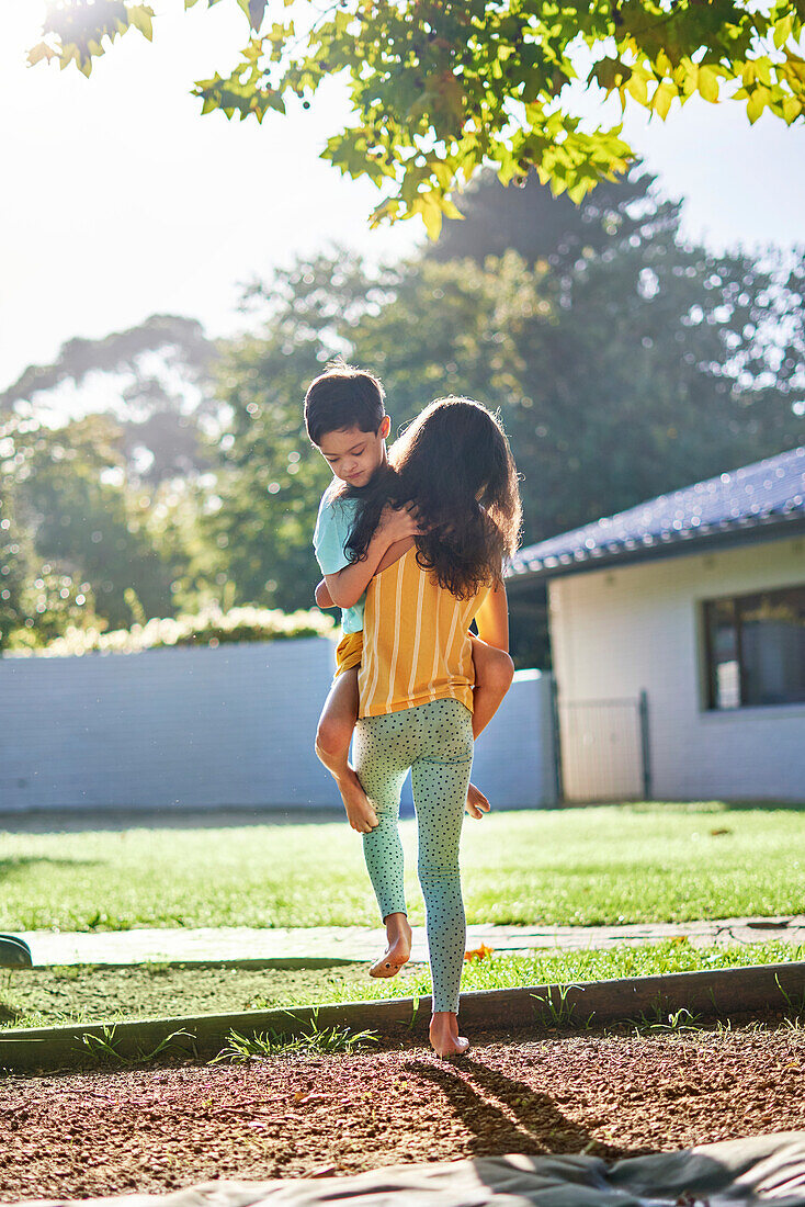 Sister carrying brother in sunny backyard