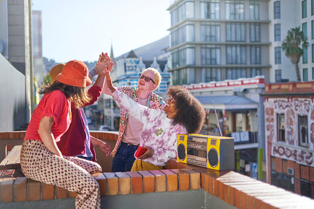 Young friends high-fiving on sunny urban city balcony