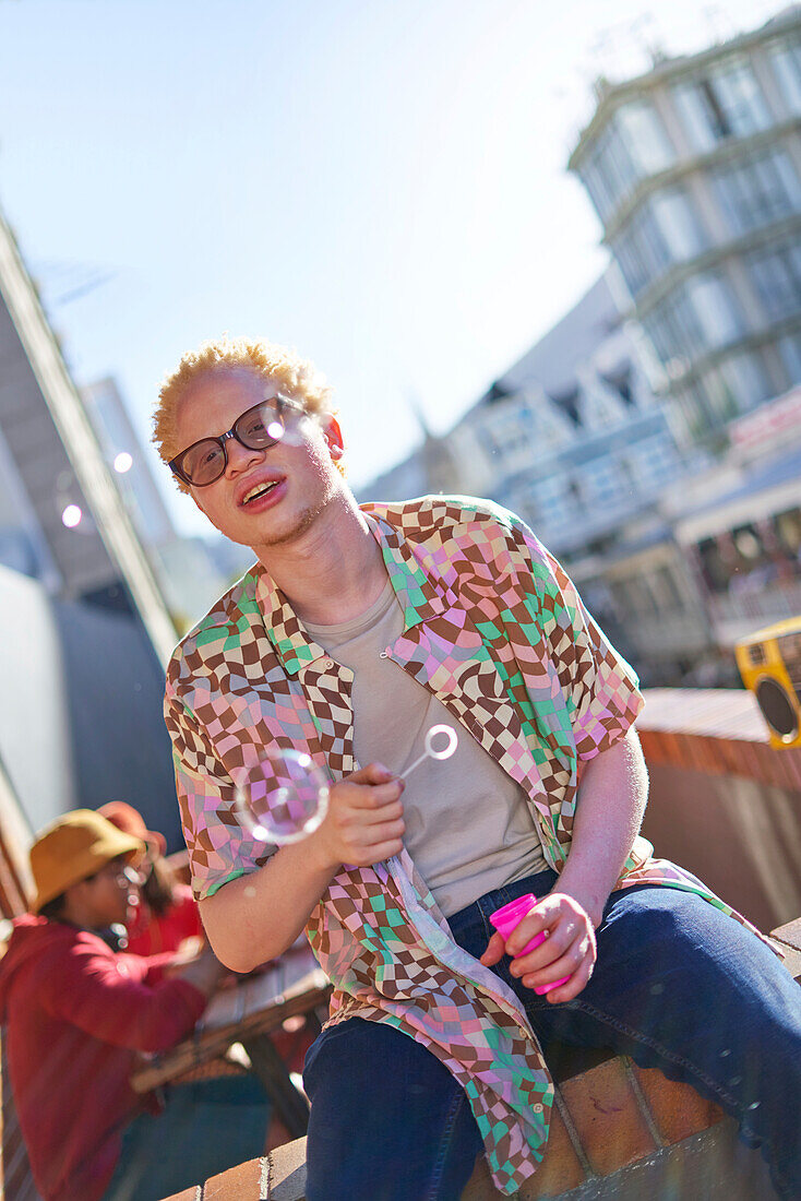 Young man blowing bubbles on sunny urban balcony