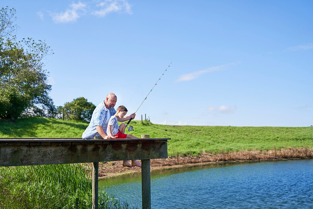 Father and son fishing on sunny lakeside dock