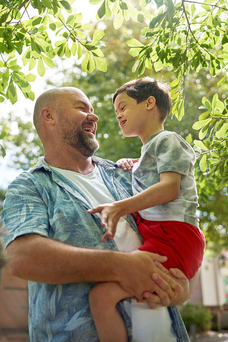 Father holding son with Down syndrome below tree