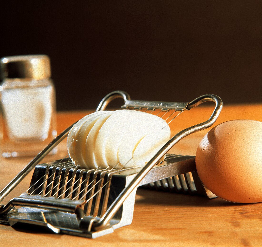 Ein gekochtes, geschältes Ei im Eierschneider, Deko: Ei, Salz