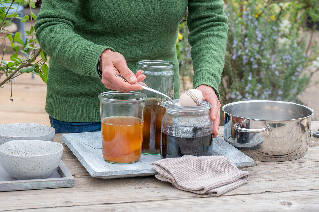 Woman dyeing Easter eggs, different colors in jars, egg wrapped with string