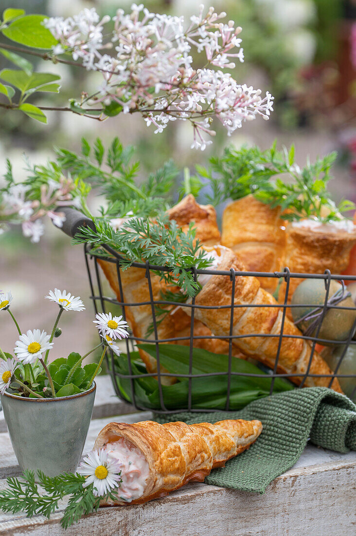 Puff pastry cones filled with carrot and dill sour cream in a wire basket, herbs as decoration, daisies in a cup as a vase