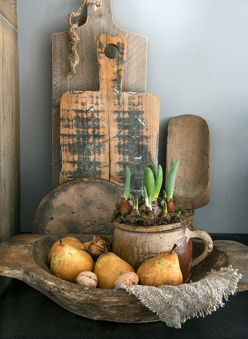 Holzschale mit Birnen und Topf mit Blumenzwiebeln vor rustikalen Schneidebrettern