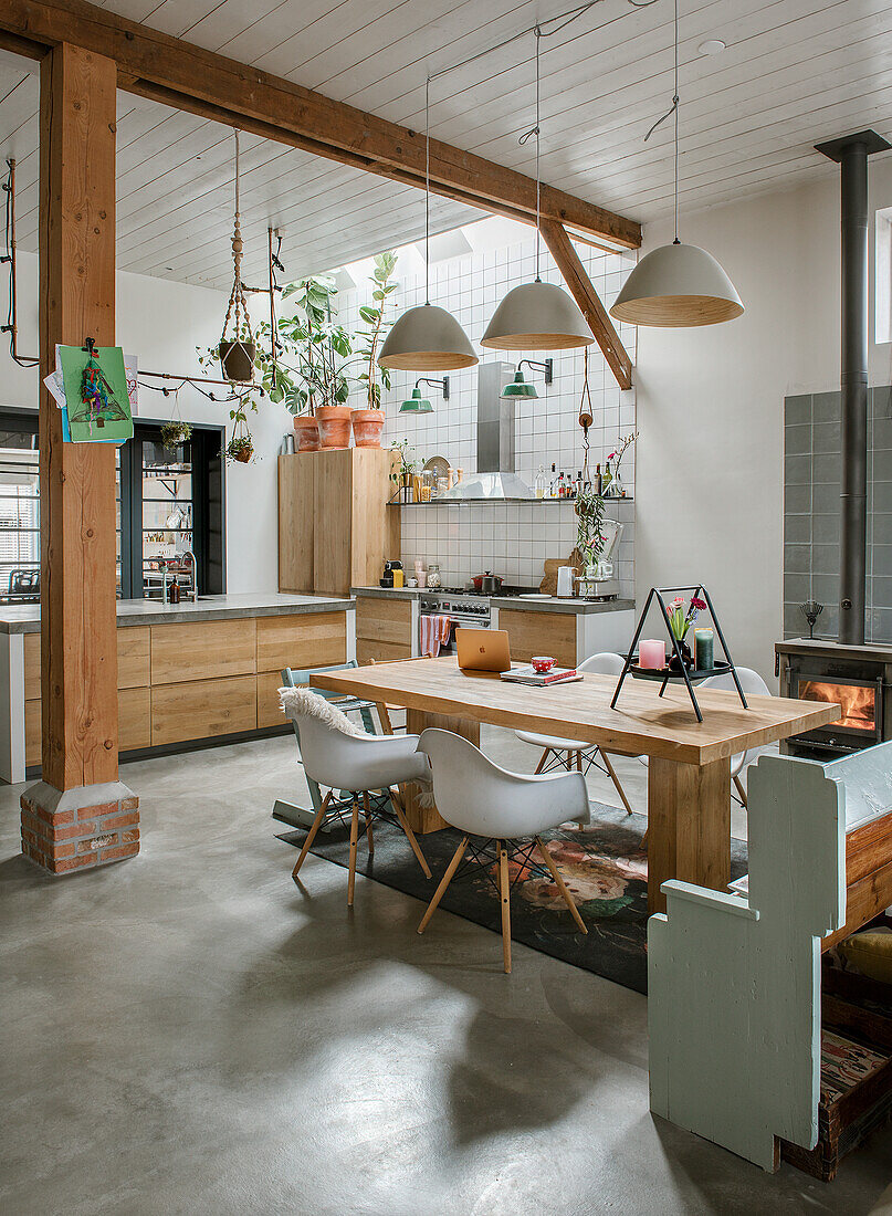 Open-plan kitchen with wooden table, white chairs and pendant lights