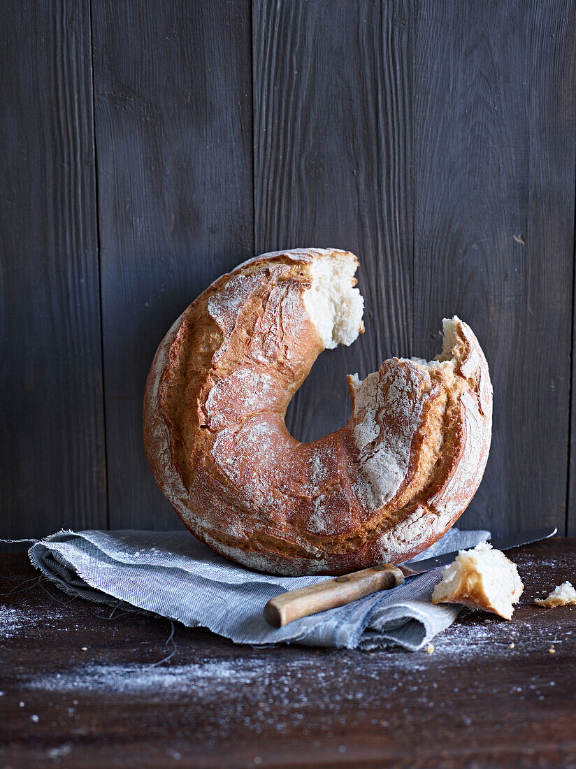 Light-coloured bread in ring shape, a piece broken out