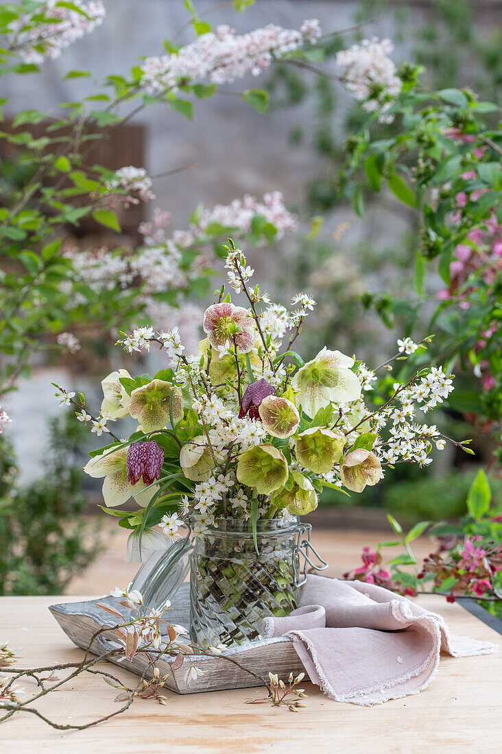 Bouquet of rock pear (Amelanchier), chequerboard flower (Fritillaria meleagris), blackthorn, purple rose (Helleborus orientalis) in vase on patio table