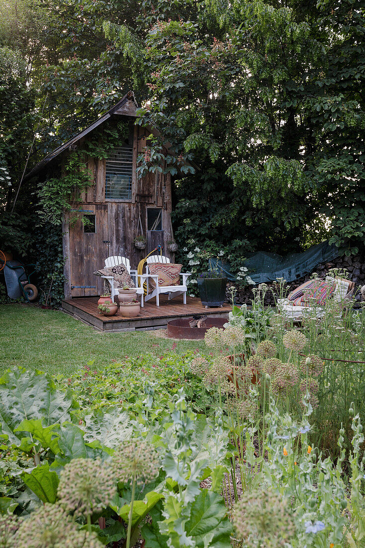 Gemütliche Gartenecke mit Holzhütte und Sesselduo, umgeben von üppigem Grün