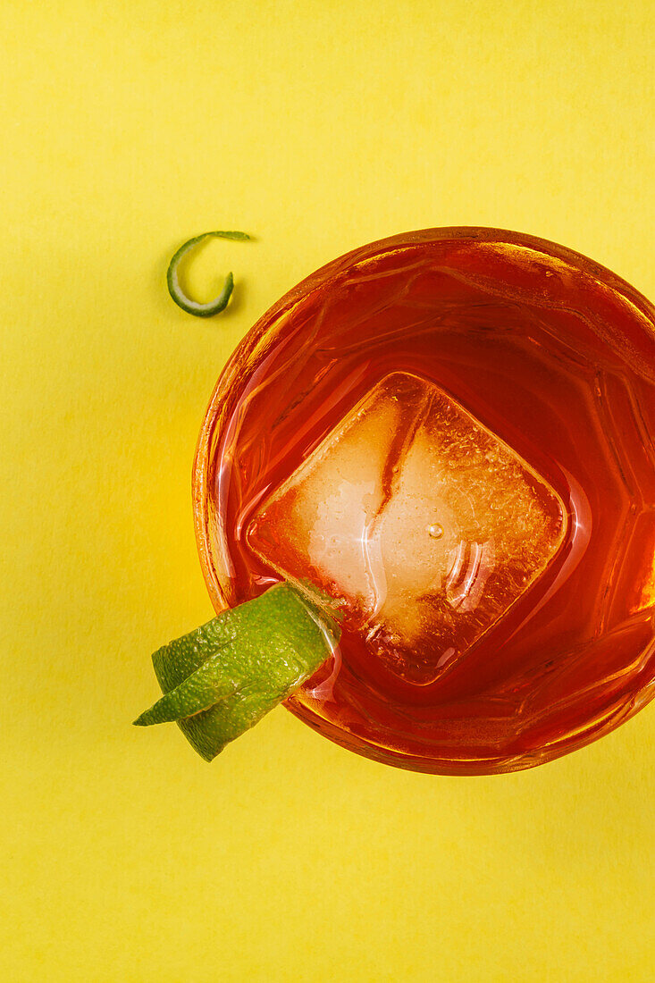 Red cocktail with ice cubes and a slice of lime