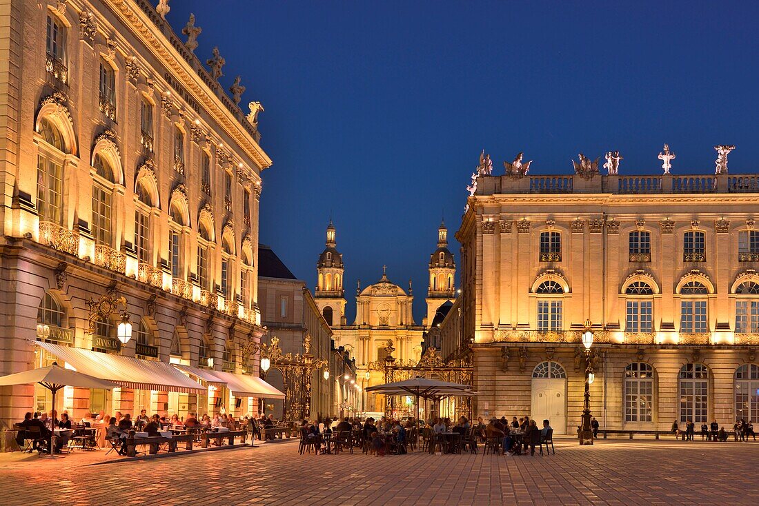 France,Meurthe and Moselle,Nancy,place Stanislas (former Place Royale) built by Stanislas Leszczynski,king of Poland and last duke of Lorraine in the eighteenth century,classified World Heritage of UNESCO,terrace of the hotel cafe Le Grand Hôtel with the cathedral Notre-Dame-de-l'Annonciation by night