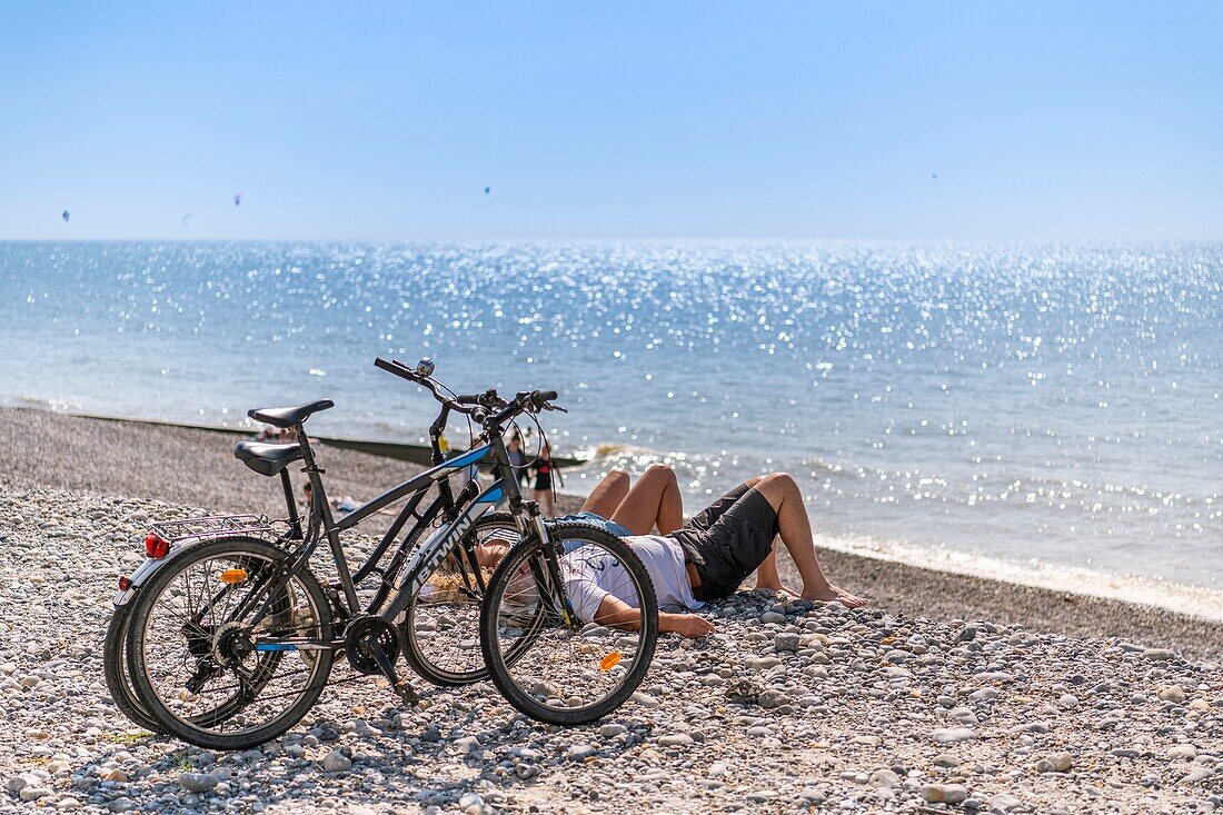 France,Somme,Cayeux sur Mer,A couple of cyclists take a nap on the pebbles facing the sea