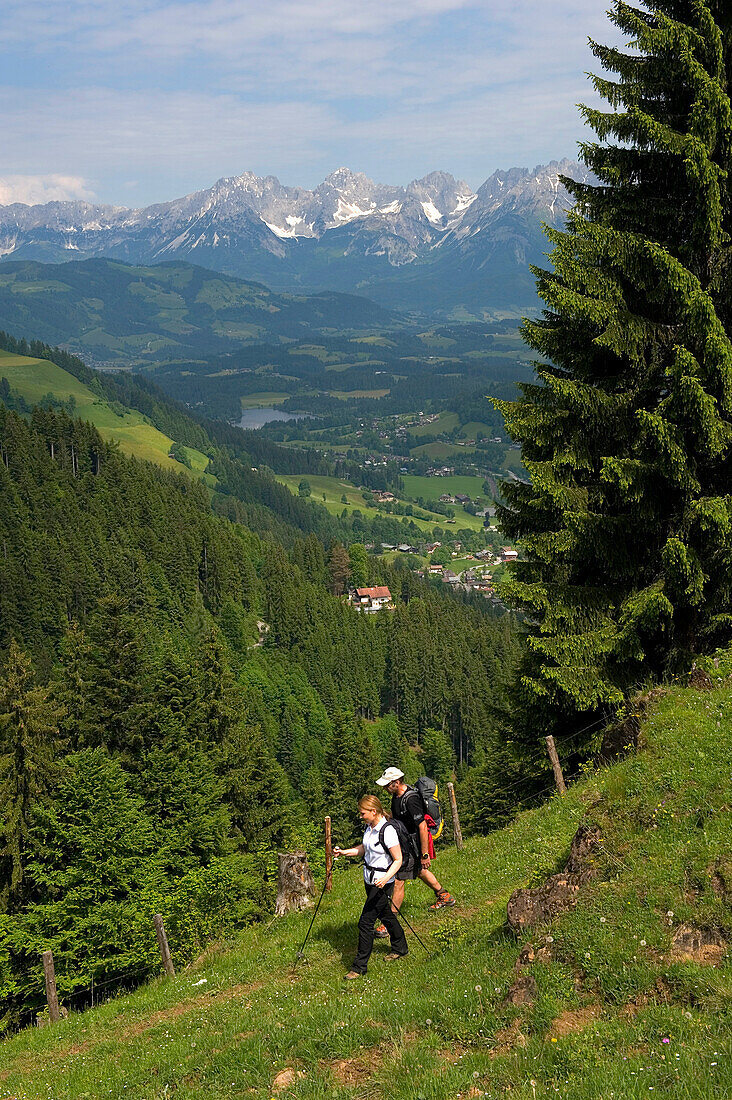 Ein Paar beim Wandern in der Kitzbüheler Alpenregion mit dem Wilden Kaiser im Hintergrund. Tirol, Österreich.