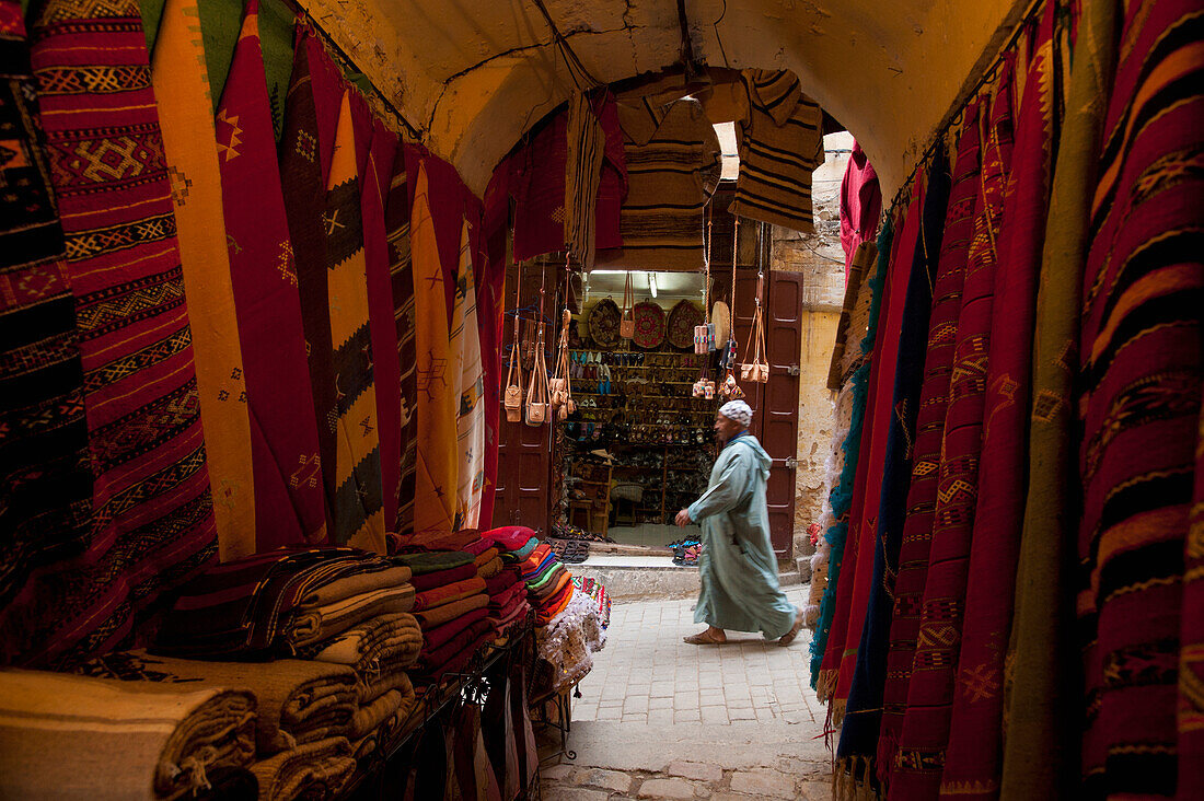 Morocco,Looking past clothes for sale in narrow passageway to man walking down alley,Fez