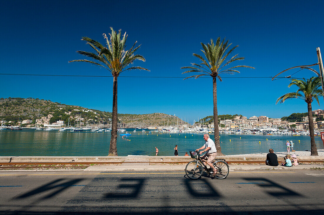 Spain,Cyclist going past shadows of letters from Eden Hotel on road in front of beach of Port Soller,Majorca