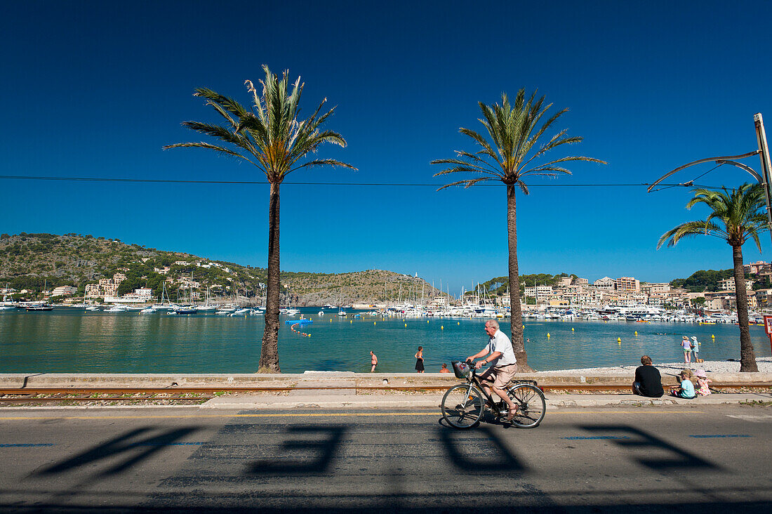 Spanien,Radfahrer fahren vorbei an Schatten von Buchstaben von Eden Hotel auf der Straße vor dem Strand von Port Soller, Mallorca